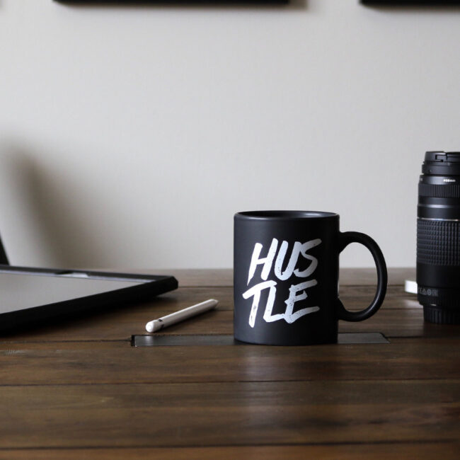 black coffee mug that says "hustle" on desk