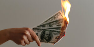 hand holding money lit on fire