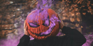 man wearing a jack-o-lantern on his head with purple smoke