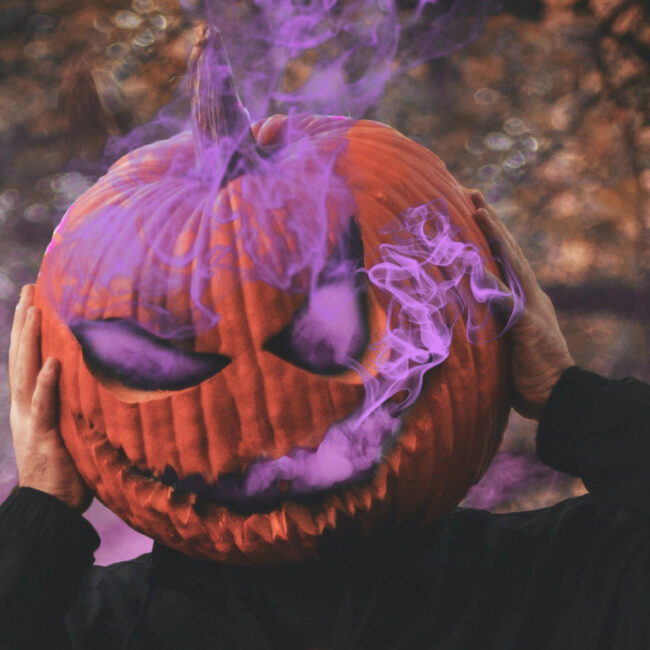man wearing a jack-o-lantern on his head with purple smoke