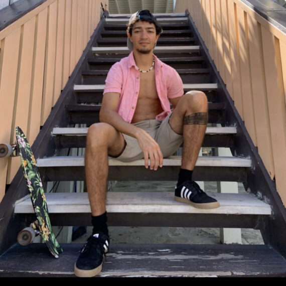 Man sitting on the stairs with a skateboard, wearing pink shirt