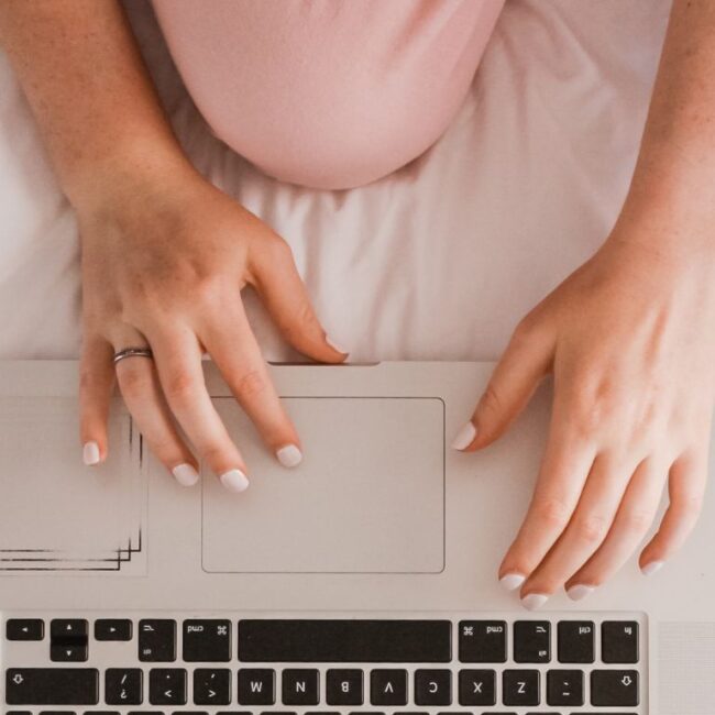 Woman wearing pink pijamas sitting in bed with her laptop