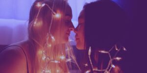 Two women about to kiss around christmas light strip