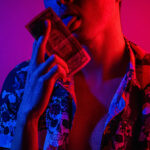 man wearing a pattern shirt licking a dollar bill