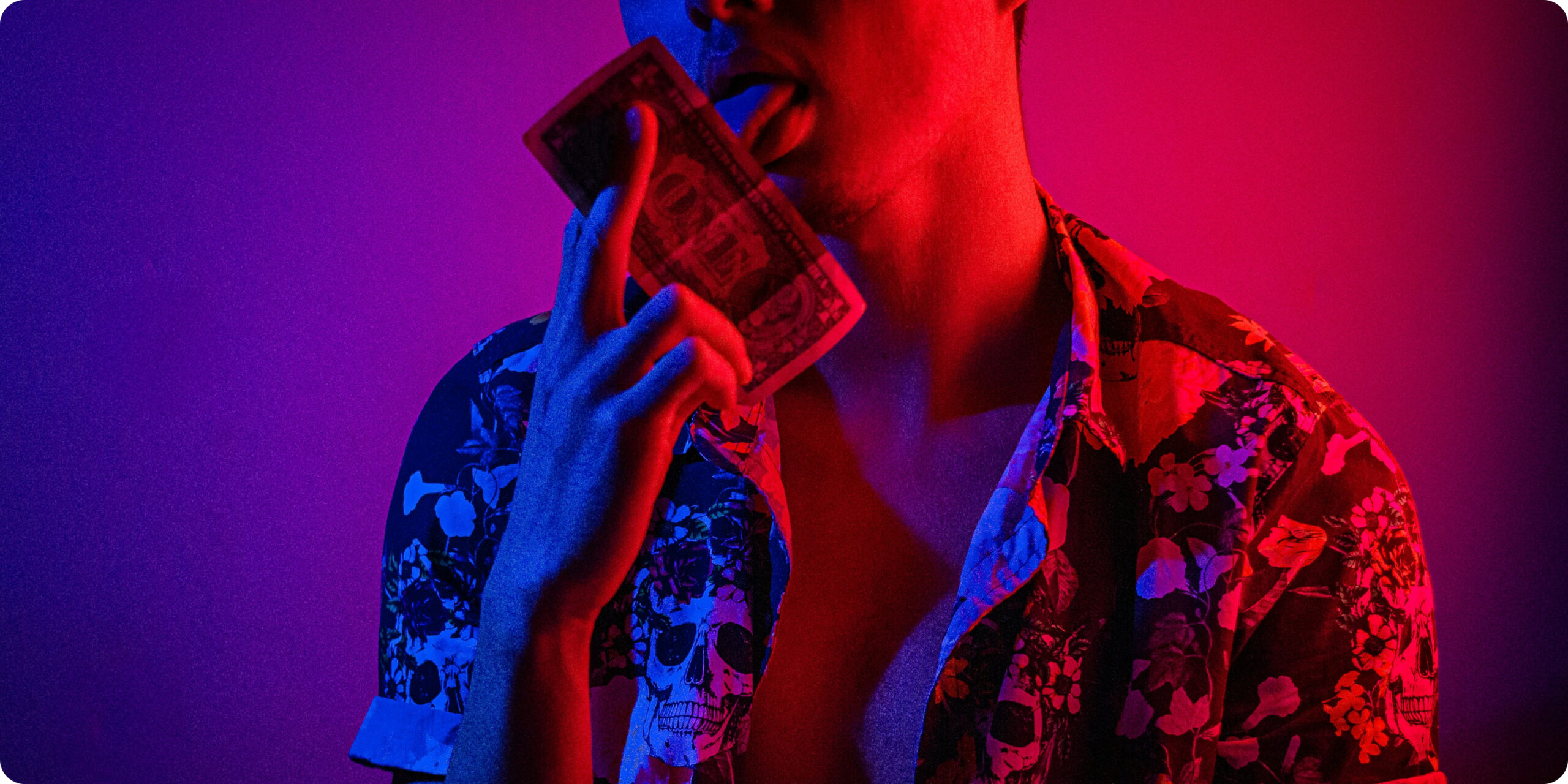 man wearing a pattern shirt licking a dollar bill