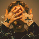 woman dressed in black with sticker shaped as crosses on her hand, cover in her face while tangled in lights