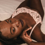 Black woman laying in bed wearing pink flowered lingerie