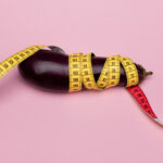 Eggplant wrapped in measuring tape on a pink background, symbolizing penis size and body image concerns.