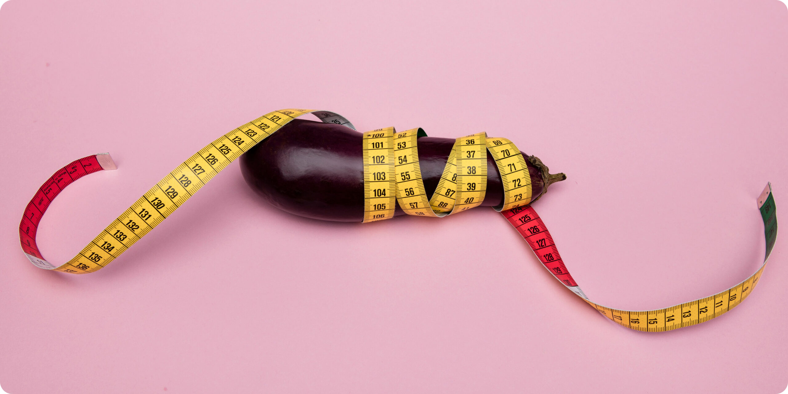 Eggplant wrapped in measuring tape on a pink background, symbolizing penis size and body image concerns.